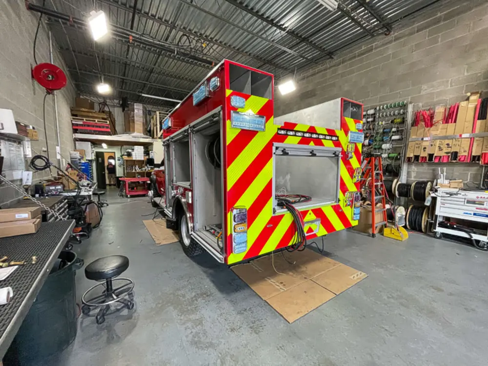 Exterior view of small fire truck showing cab, body compartments, and wheel/tire area.